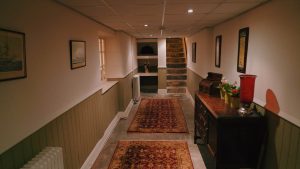 A cozy hallway in the lower level of Noblethorpe Hall in Silkstone, Barnsley, featuring sage green wall paneling, oriental rugs on a stone floor, and a set of historic stone stairs leading upwards.